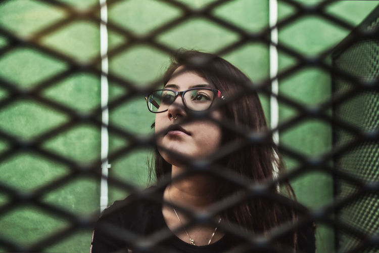 Close-up portrait of young woman behind fence