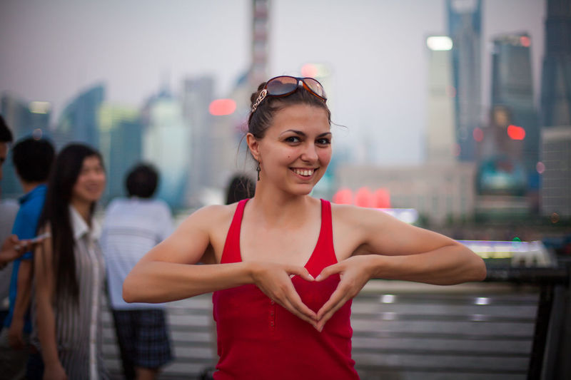 Portrait of happy woman making heart shape with hands in city