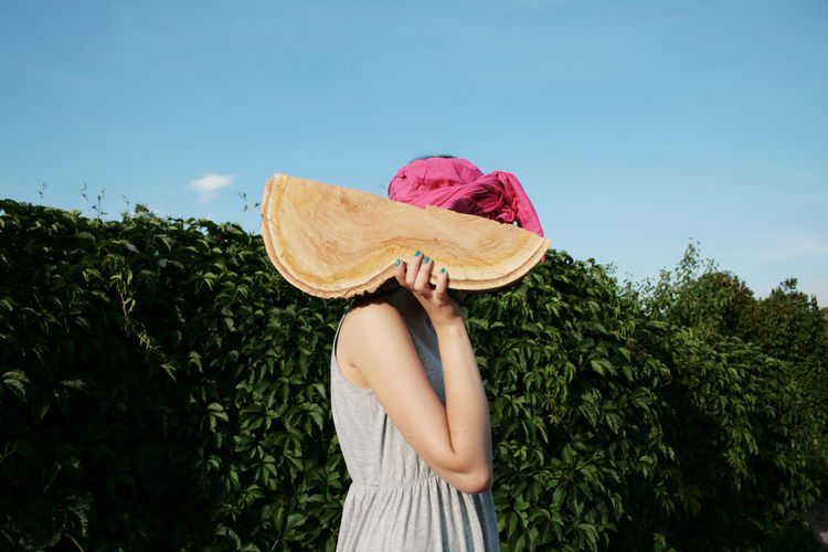 Woman holding wood while standing against hedge
