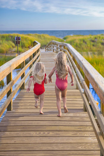 Little girls from behind running on bridge to beach