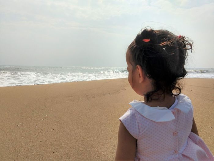 Child watching sea waves first time at  a beach against sky