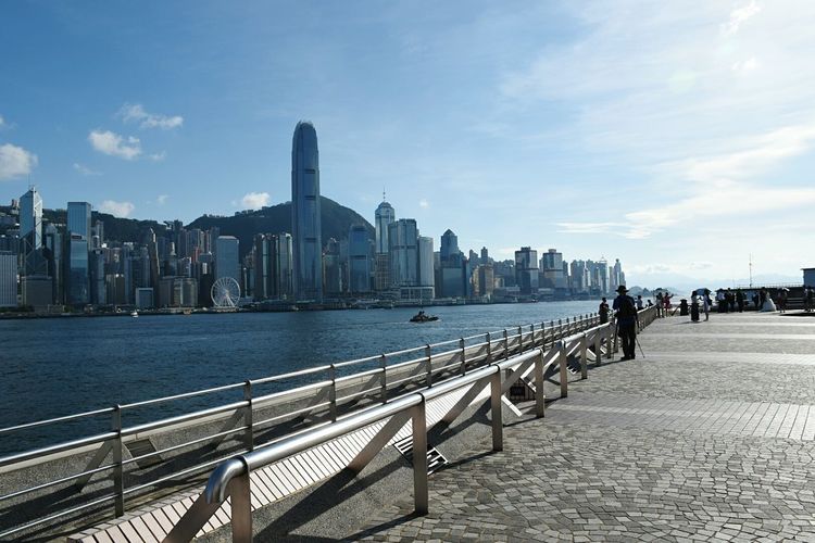 Two international finance center amidst buildings in front of sea and walkway on sunny day