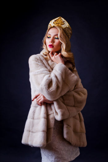 Beautiful woman wearing fur jacket and crown against black background