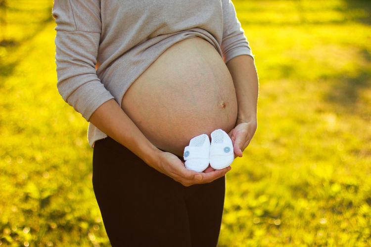 Midsection of pregnant woman holding baby booties while standing on field