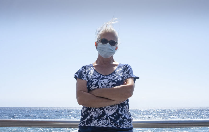 Senior woman wearing sunglasses against sea against clear sky