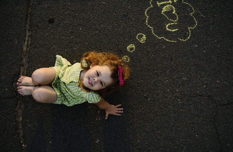 Directly above portrait of cute girl sitting by chalk drawing on road