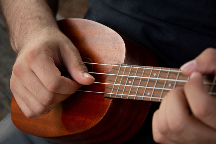 Cropped hand of man playing ukulele outdoors