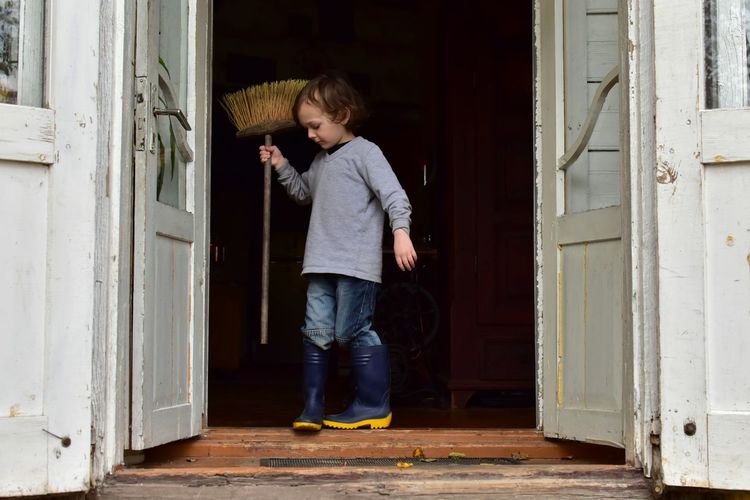 Full length of boy holding broom on doorway
