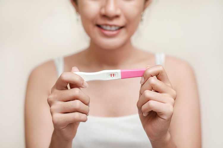 Midsection of woman holding pregnancy test while sitting against wall