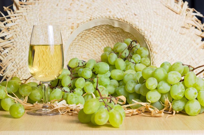 Close-up of grapes and wineglass on table against wicker hat