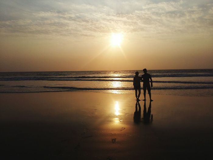 Silhouette of couple standing at beach against sky during sunset