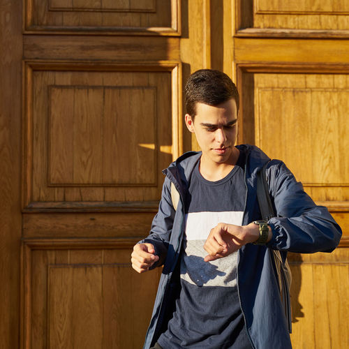 Young man looking away while standing against wooden wall