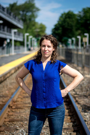 Portrait of woman with hands on hip while standing at railroad track