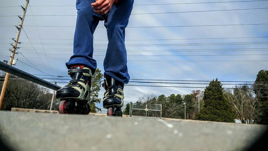 Low section of man standing on roller skate against sky during sunny day