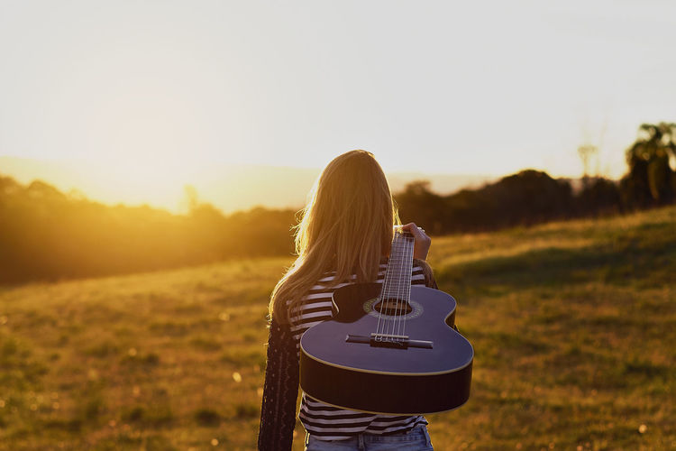 Rear view of woman with guitar on field