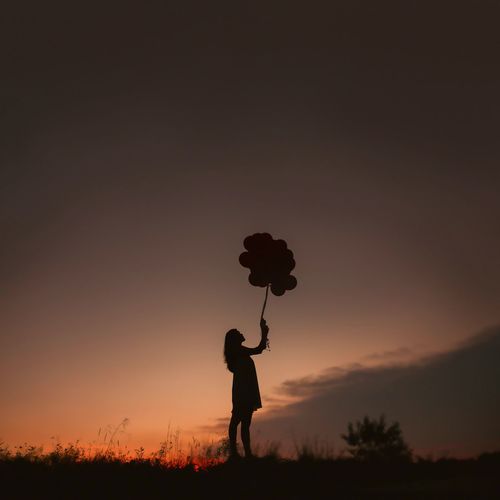 Silhouette of young woman holding balloons