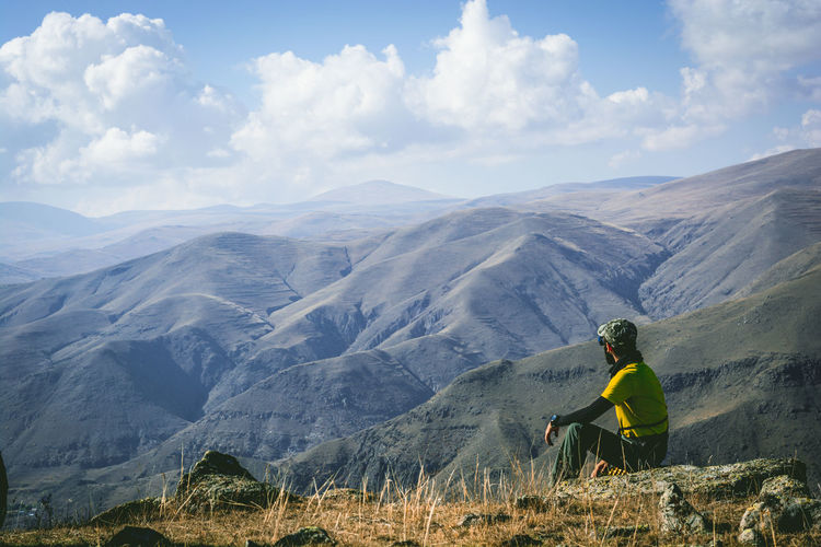 Man sitting on cliff against mountains