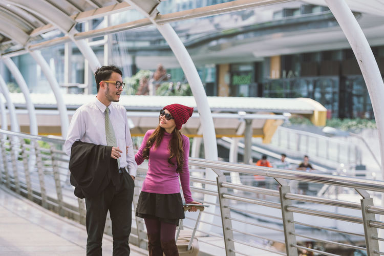 Businessman and woman standing with luggage by railing on footbridge