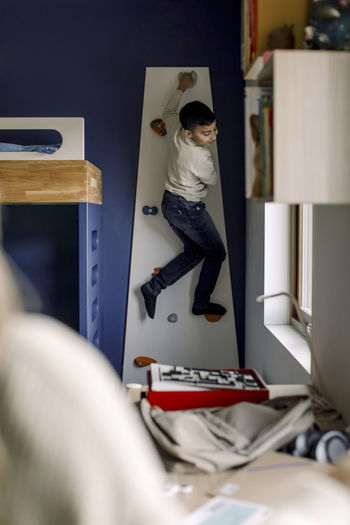 Pre-adolescent boy climbing wall in bedroom