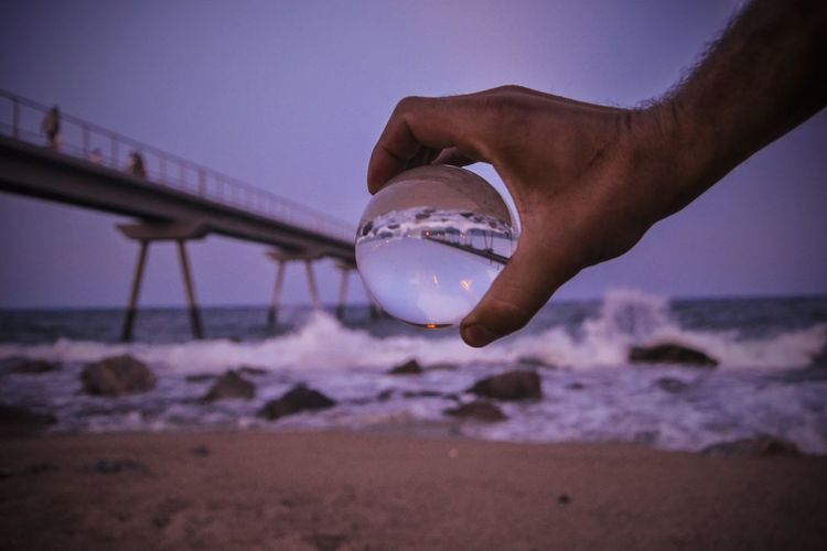 Close-up of hand glass ball at beach against sky