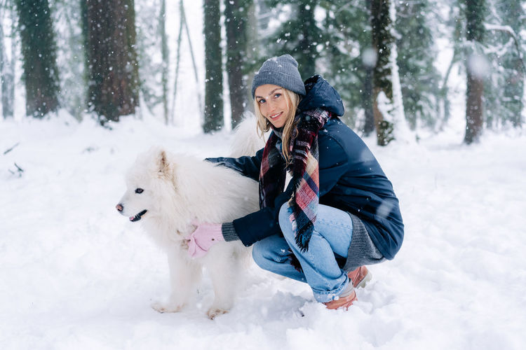 A young woman walks a dog in the park on a winter snowy day.