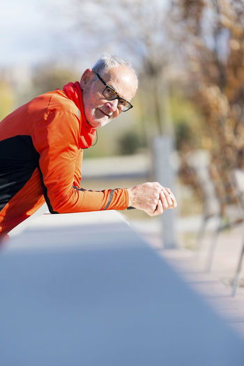 Portrait of senior man leaning on wall in park