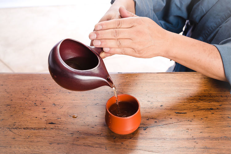 Close-up of hand pouring coffee cup on table