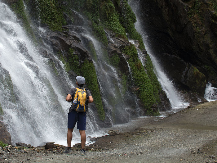 Full length of man standing on rock against waterfall