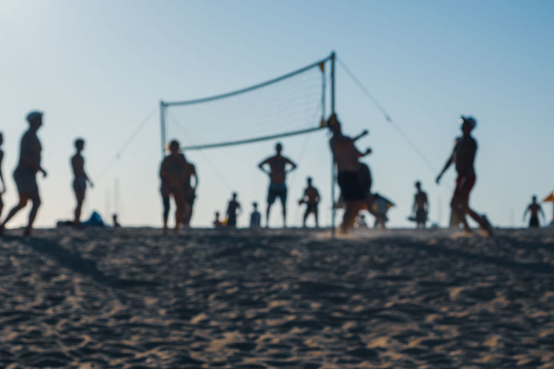 People playing ball on beach against clear sky