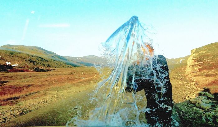 Close-up of man splashing water on field against clear sky