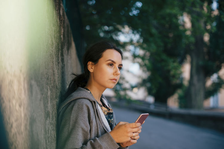 Portrait of young woman using mobile phone against tree