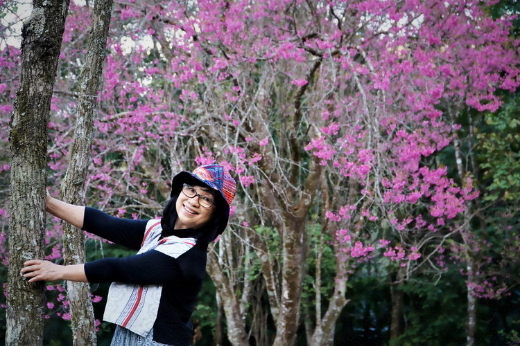 Smiling woman standing by pink flowering tree