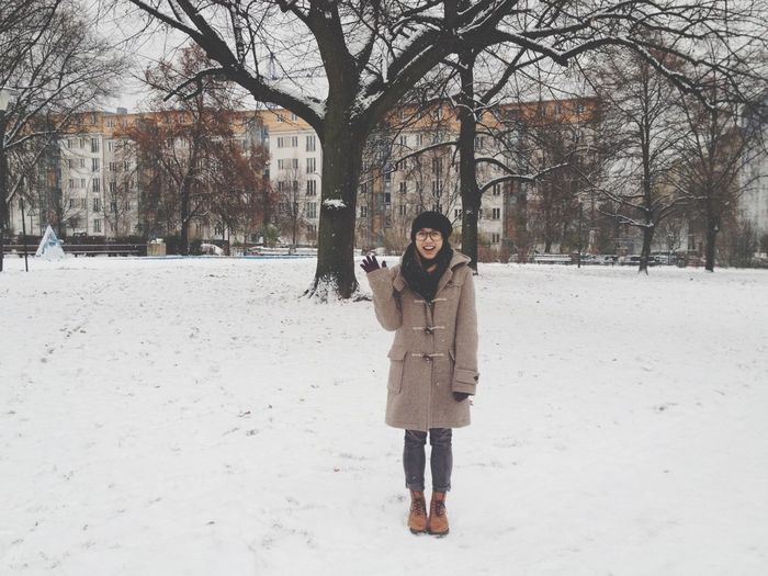 Happy woman standing on snow covered park against bare trees and buildings