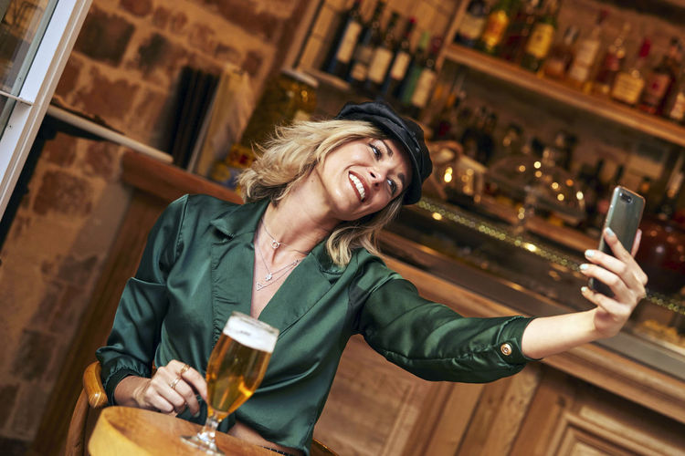 Cheerful woman doing selfie while sitting at bar