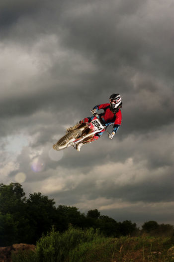 Low angle view of biker performing stunt in mid-air against cloudy sky