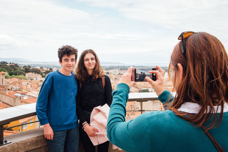 Woman photographing with mobile phone against sky