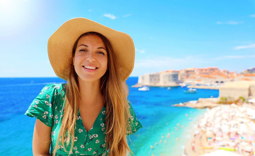 Portrait of smiling young woman at beach against sky