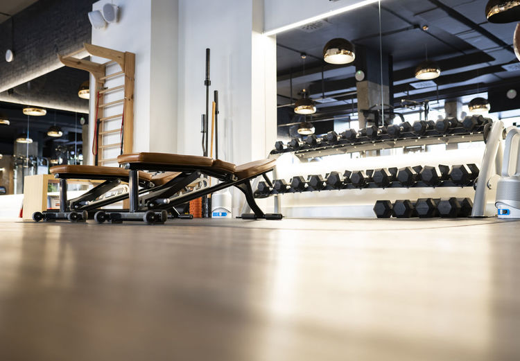 Leather benches and rack with various dumbbells located inside contemporary gym for weightlifting workout