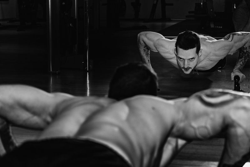 Rear view of shirtless man exercising against mirror at gym