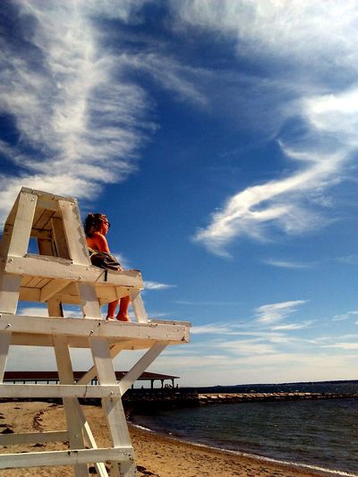 Low angle view of woman sitting on lifeguard chair at beach