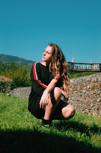 Teenage girl crouching on field against clear sky