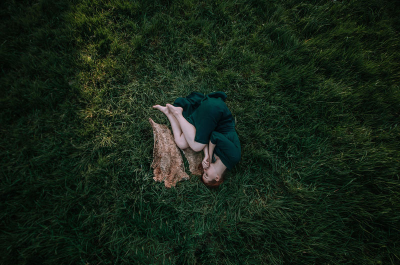 HIGH ANGLE VIEW OF WOMAN LYING ON GRASS FIELD