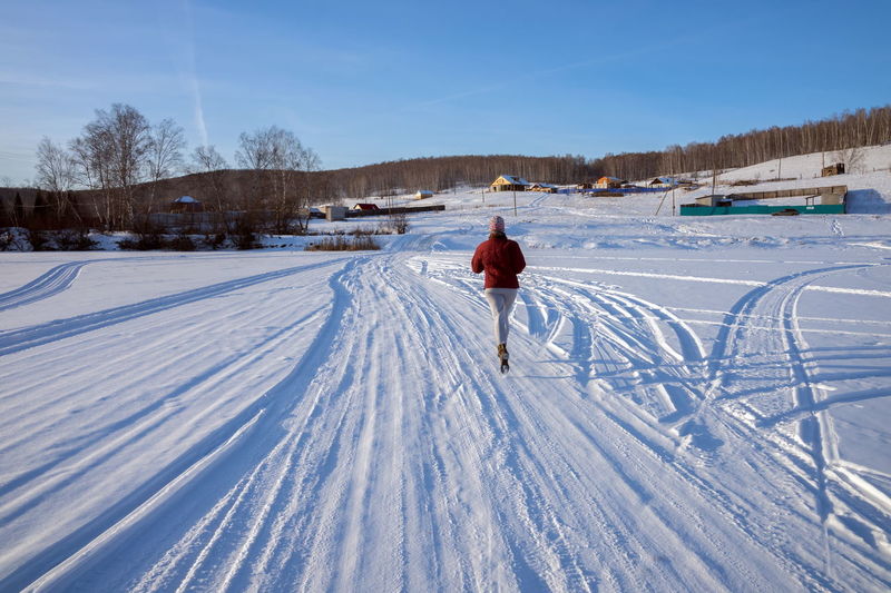 Girl runs along a winter road on a frozen lake towards a village on a hill, on a winter sunny day.