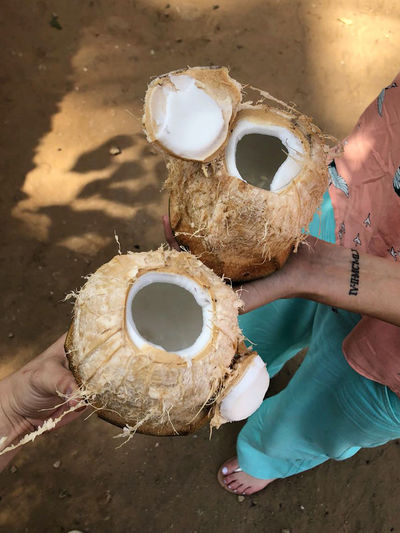 Two people holding open fresh coconuts in theo hands in a sand floor