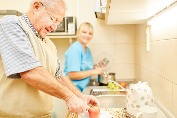 Man cutting apple with nurse preparing food in kitchen