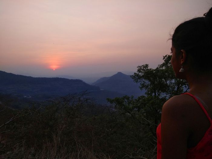 Side view of woman looking at mountains against sky during sunset