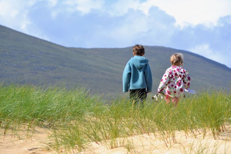 Rear view of children on sand dunes  against sky