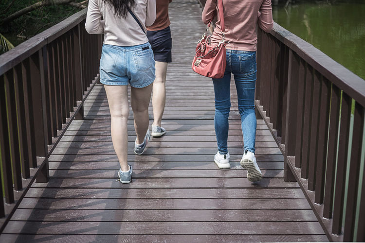Low section of friends walking on footbridge