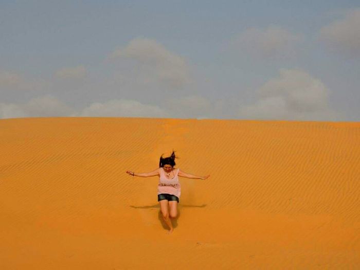 Woman jumping at desert against sky