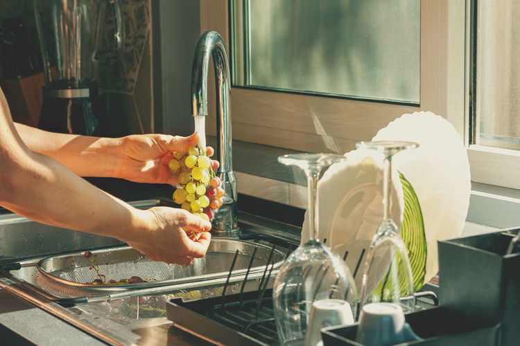 Female hands washing bunches of harvested ripe and juicy green grapes in the kitchen. 